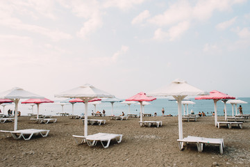 white sunbeds with colorful umbrellas on a pebble beach in the summer