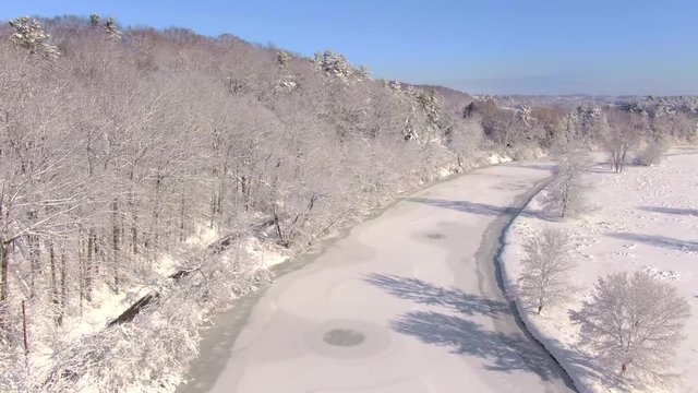 Beautiful river amid snow covered Winter wonderland landscape, aerial drone view.