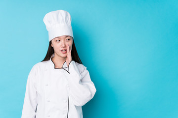 Young chinese chef woman isolated is saying a secret hot braking news and looking aside