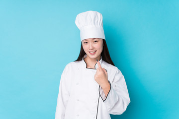 Young chinese chef woman isolated pointing with finger at you as if inviting come closer.