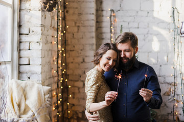 Celebrating Christmas together. Young caucasian couple in holiday clothes hugging near the Christmas tree. New Year, Valentine, love, romance concept.