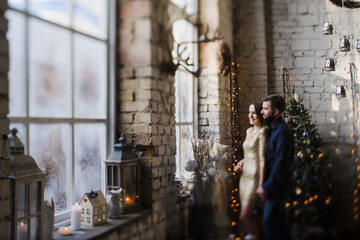 Obraz premium Celebrating Christmas together. Young caucasian couple in holiday clothes hugging near the Christmas tree. New Year, Valentine, love, romance concept.