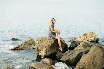 a young beautiful girl in a dress on large stones, a picturesque place on the sea coast