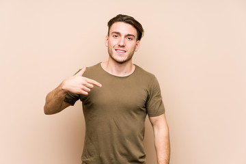 Young caucasian man posing isolated person pointing by hand to a shirt copy space, proud and confident