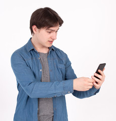 Surprised young man holds smartphone in blue shirt looking into the mobile phone.