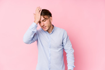 Young caucasian man posing in a pink background isolated forgetting something, slapping forehead with palm and closing eyes.