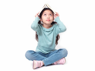 Asian little cute girl 6 years old sitting on floor and put the book on head. Preschool lovely kid with the book covering on her head. Learning and education of kid.