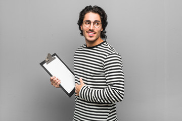 Young employee man holding an inventory looks aside smiling, cheerful and pleasant.