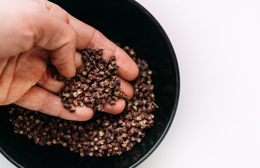 Man's palm taking a scented Sichuan pepper from the bowl on the white table. Sichuan pepper or Chinese pepper or Timur or Nepali pepper is very popular in cuisines of Tibet, Bhutan, Nepal, Thailand.