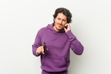 Young man holding a vaporizer covering ears with hands.