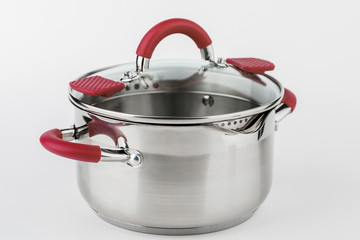 Stainless casserole with glass lid and red handles on grey background.