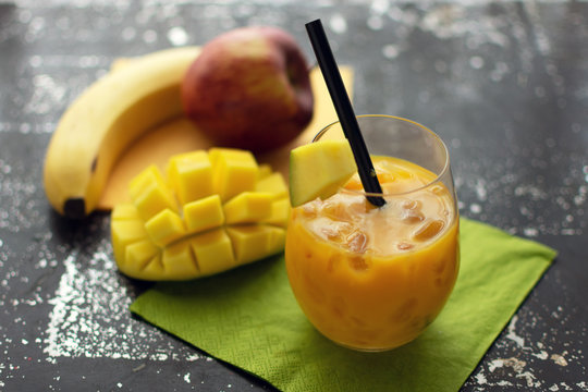 leckerer Smoothie mit Mango im  Glas mit crushed ice und Strohhalm. Im Hintergrund liegen frische Früchte
