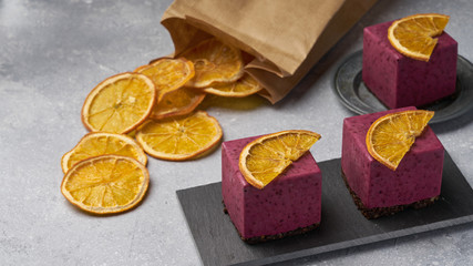 raw currant cheesecake a square cake with a slice of dried orange on a gray concrete background