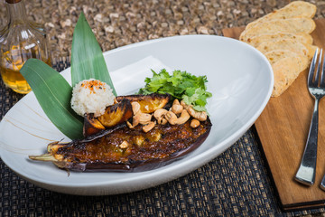 Asian cuisine, baked eggplant with nuts and rice in a deep plate on a table in a restaurant.