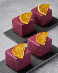 raw currant cheesecake a square cake with a slice of dried orange on a gray concrete background