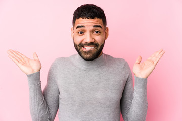 Young latin man against a pink background isolated confused and doubtful shrugging shoulders to...