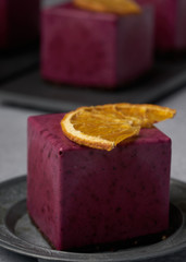 raw currant cheesecake a square cake with a slice of dried orange on a gray concrete background