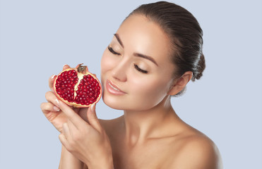 Portrait of a smiling woman with clean skin holds ripe pomegranate near the face. Cosmetology skin...