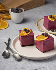 raw currant cheesecake a square cake with a slice of dried orange on a gray concrete background
