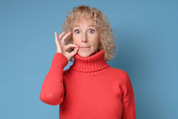 Beautiful caucasian mature woman shutting mouth and lips shut as zip with fingers. Secret and...