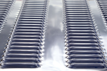 Repeating rows of cooling holes on a chrome metal surface of the hood of a modern car.