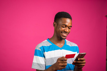 young handsome nigerian man isolated over pink background making transaction online with is smart...