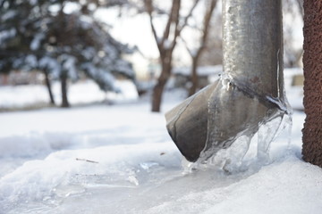 Drainpipe covered with ice on the corner of the house.