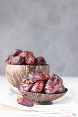 Coconut shell with organic medjool dates on a light grey concrete background. Selective focus, copy space.