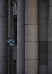 Clock hanging on a building with concrete columns and a facade