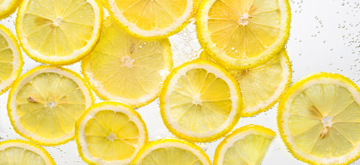 Slices of lemon in water with air bubbles on white background.