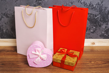 red and pink paper shopping bags and two gift boxes on the wooden floor against a concrete wall...