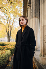 Beautiful stylish girl in black coat intently looking away on beautiful street