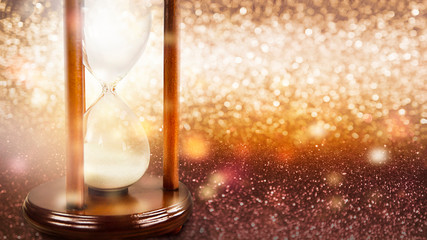 Vintage wooden hourglass retro clock on festive golden bokeh shiny background. Copy space....