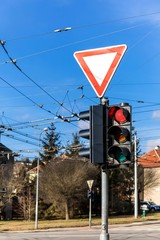 Traffic light at city intersection. Power line for trolleybus. Stop light signal. Road sign give way. City of Brno Czech Republic.