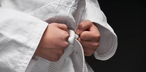 Zelfklevend Fotobehang hands closeup - teenager dressed in martial arts clothing posing on a dark gray background, a sports concept © soleg