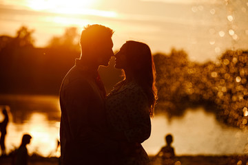 silhouette of loving couple hugging on the lake at sunset. Beautiful young couple in love walking...