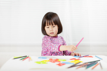 toddler girl practice writing letters on white paper against white background