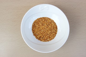 Ground garlic in a white  bowl isolated on a wooden table. Soft focus at the background