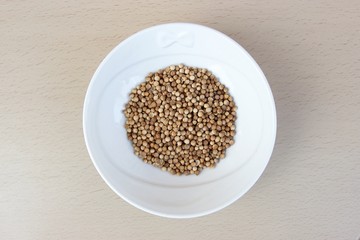 Coriander seeds in a white ceramic bowl isolated on a wooden table from above. Soft focus at the background