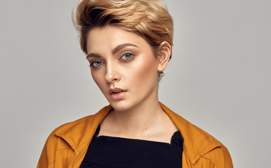 Close up face of young female model with blue eyes and short blonde hair isolated on gray background