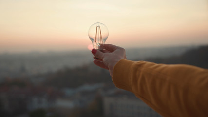 Close up hands woman holds a house light bulb at sunset renewable energy nature electricity...