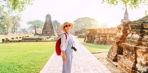 Young backpacker Tourist woman with a modern mirrorless camera enjoying walking at ancient ruins during her Asian vacation, Ayutthaya, Thailand. - obrazy, fototapety, plakaty
