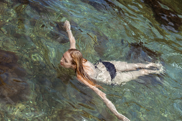 Beautiful slim young woman in a black bikini swimsuit resting on a rocky beach