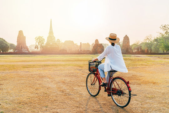 Woman riding a bicycle with front basket  near Ayutthaya historical park in Thailand, a beautiful early morning time with bright sunrise light. Careless Asian vacation concept image.