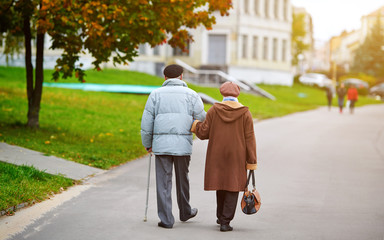 Senior couple walking in the city street. Senior elderly couple walking hand in hand, the man with...