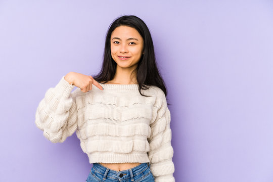 Young chinese  woman isolated on a purple background person pointing by hand to a shirt copy space, proud and confident