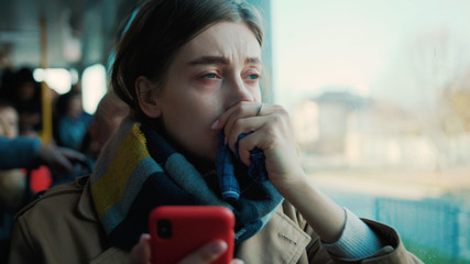 Young woman use phone headache feel bad on the tram cold autumn day flu season disease fever grippe...