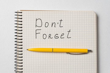 Don't Forget reminder notice. Words handwritten. Notebook and pen on a white background.