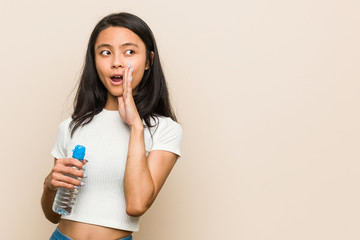 Young asian woman holding a water bottle is saying a secret hot braking news and looking aside