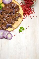 fresh chunks of beef liver on a cutting Board next to onions and spices on a wooden white table selective